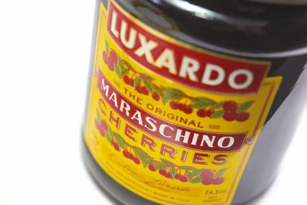 Close-up of a Luxardo jar label for The Original Maraschino Cherries, with vibrant red cherries on a bright yellow background.