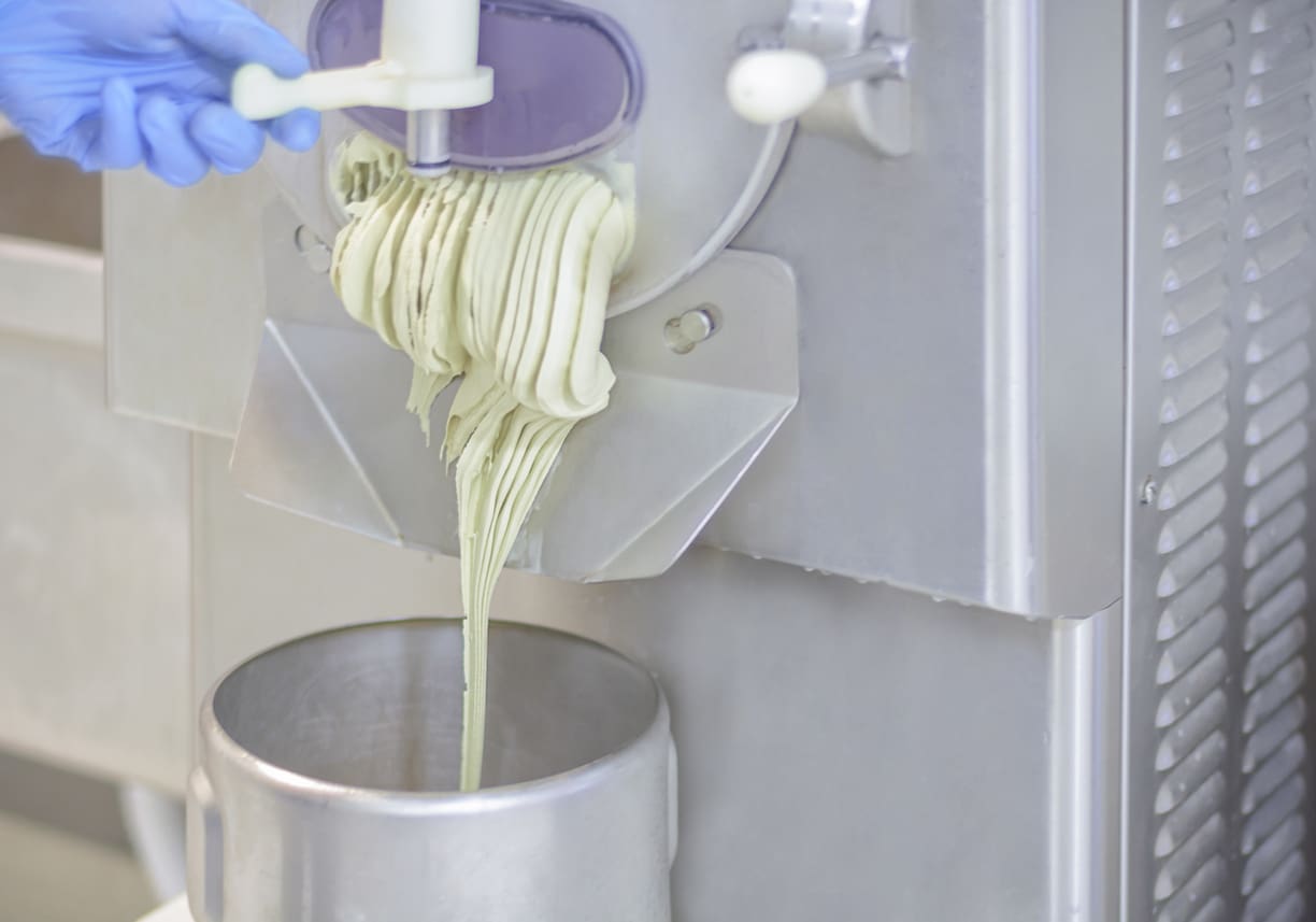 Freshly squeezed juice pouring from a manual juicer into a metal cup.