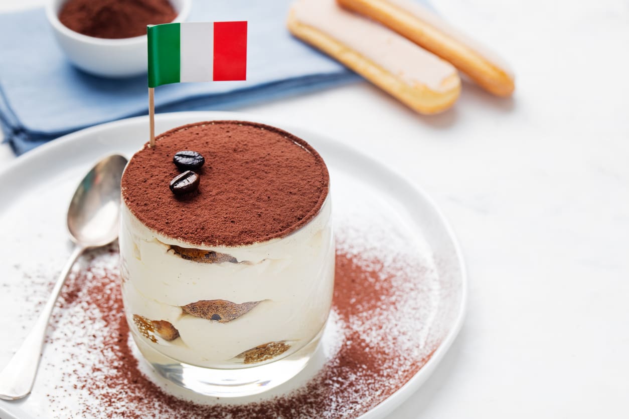 Glass of tiramisu dessert with Italian flag and ladyfinger biscuits.