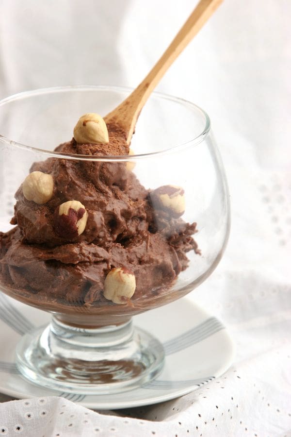 A glass bowl of rich, creamy chocolate mousse features a topping of Elenka Baci Italian Kiss Hazelnut Nut Pastes #430. A wooden spoon suggests it's ready to serve, as it rests on a saucer against a softly lit white background.