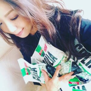 A person with long hair smiling and holding multiple packets of golia licorice candy.
