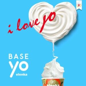 Swirl of yogurt forms a heart shape above a fruit-topped Elenka yogurt cup against a bright blue background. Red text reads "i love yo.