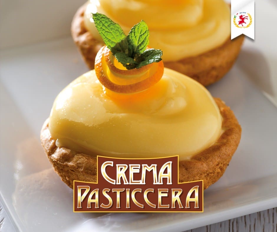 Two tarts filled with creamy custard, topped with orange slices and a mint leaf. The text "Crema Pasticcera" is displayed at the bottom. The background is a light-colored plate.