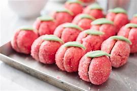 Rows of peach-shaped cookies coated in pink sugar with green icing leaves sit neatly on a tray, their vibrant color inspired by Luxardo Alkermes Aroma 70% Alcohol (2x5Li case).