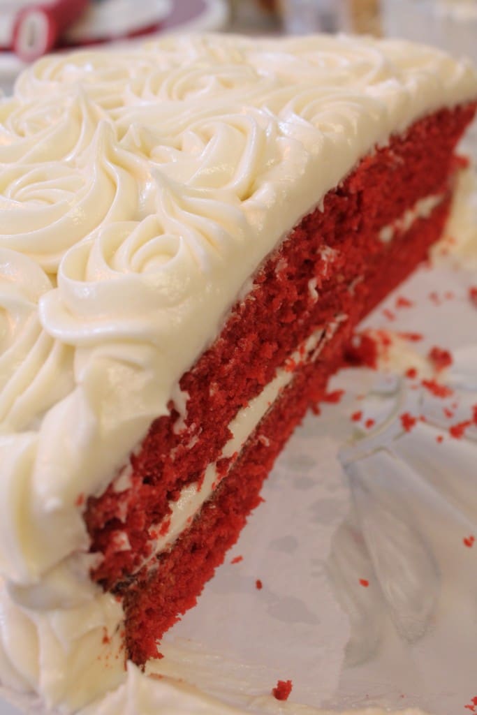 A close-up of a sliced red velvet cake with two layers, swirled cream cheese frosting, and scattered crumbs. A hint of Luxardo Alkermes Aroma 70% Alcohol (2x5Li case) adds subtle aroma to this decadent treat.