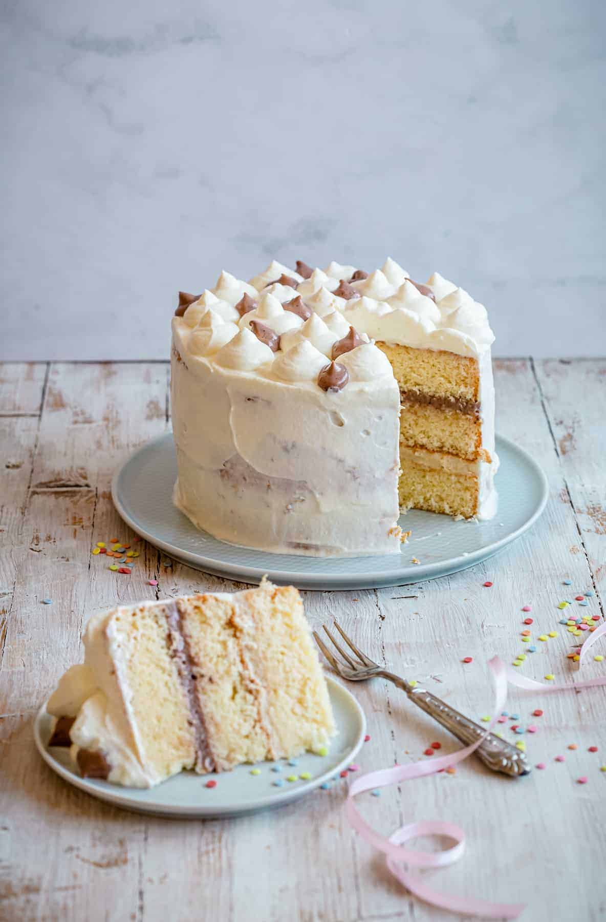 A three-layer vanilla cake with white frosting sits on a plate, inspired by the festive spirit of Benevento and perfectly paired with Luxardo Lacrime Dβoro (Benevento) Intense Aroma 70% Vol., sold in 2x5Li cases.