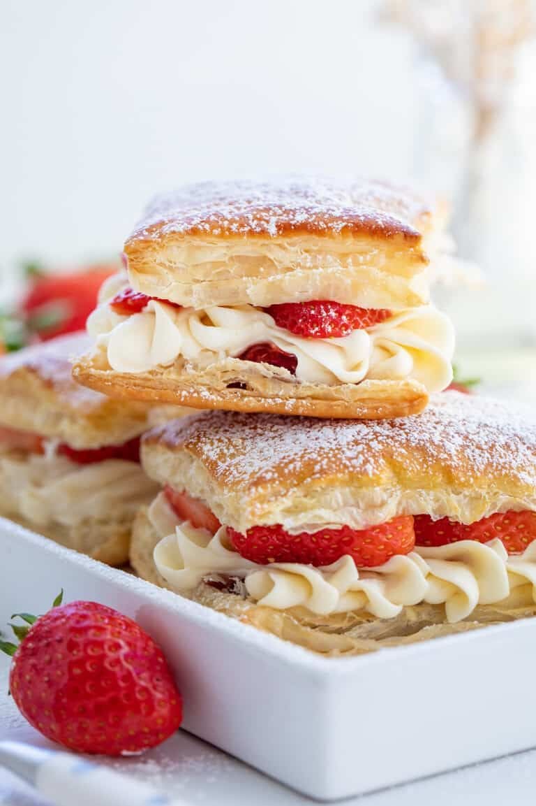 Three strawberry cream puffs with golden pastry, piped cream, and fresh strawberries, dusted with powdered sugar, are stacked on a white dishβa perfect pairing for Luxardo Lacrime D'oro (Benevento) Intense Aroma 70% Vol. Alcohol.
