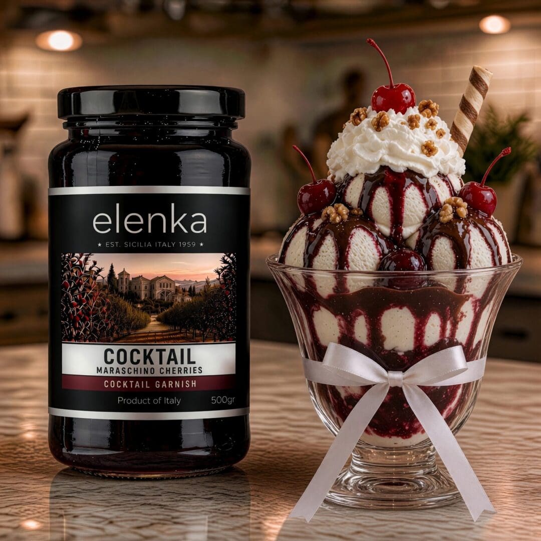 A jar of Elenka maraschino cherries sits beside a sundae topped with whipped cream, cherries, sauce, nuts, and a wafer, garnished with a ribbon, on a marble countertop in a softly blurred kitchen.